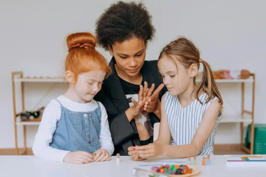 Afbeelding van een mbo-student die samen met twee kinderen van 8 tot 12 jaar een creatieve activiteit uitvoert aan tafel.